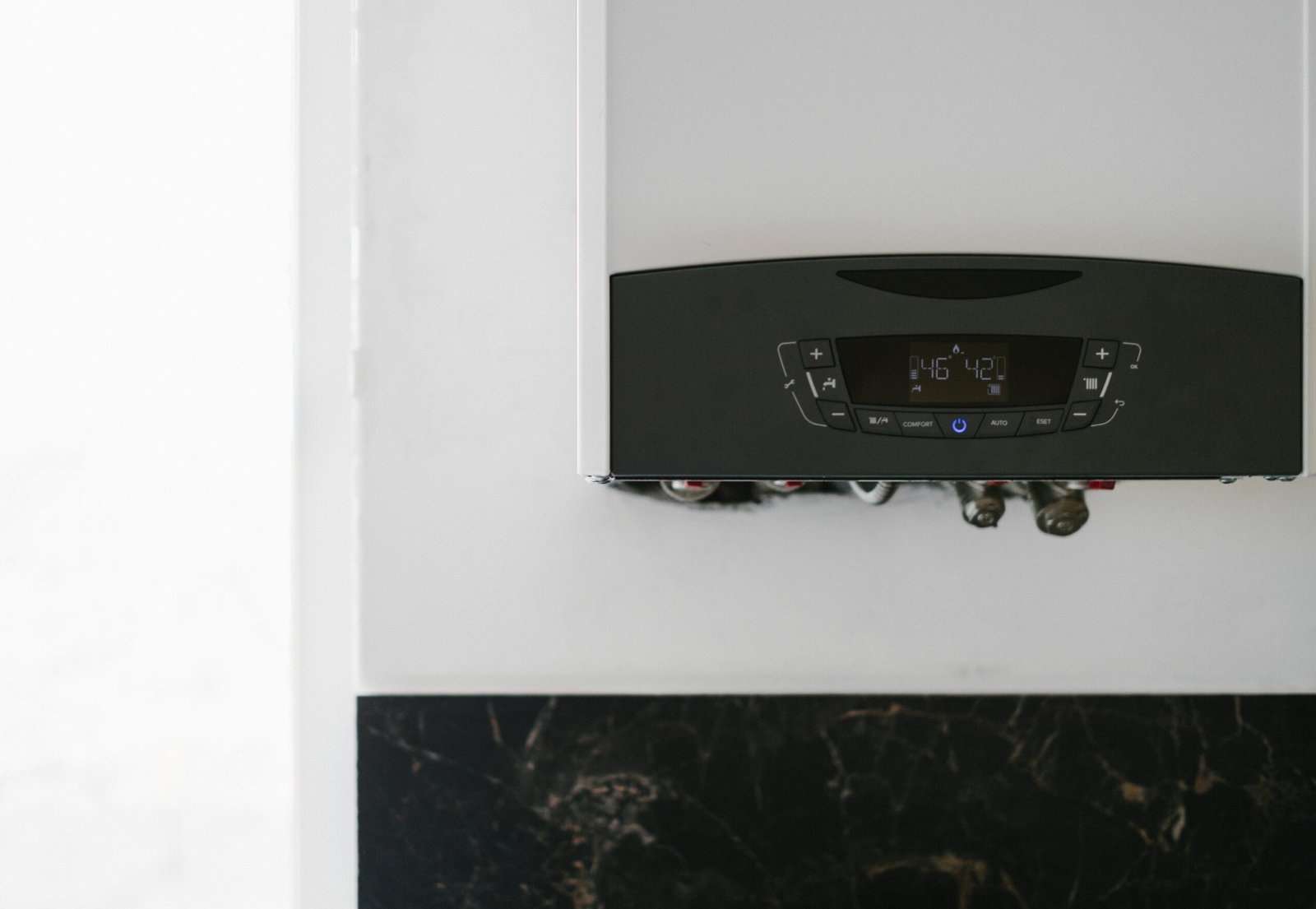 A modern, energy-efficient combi boiler newly installed on a white wall with neat copper pipework underneath.
